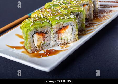 Sushi setzt Uramaki, California, Philadelphia, auf einen weißen Teller. In der Nähe Ingwer und Wasabi. Sojasauce in einer weißen Schüssel. Auf einem dunklen Hintergrund. Speicherplatz kopieren. Stockfoto