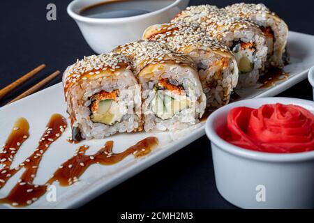 Sushi setzt Uramaki, California, Philadelphia, auf einen weißen Teller. In der Nähe Ingwer und Wasabi. Sojasauce in einer weißen Schüssel. Auf einem dunklen Hintergrund. Speicherplatz kopieren. Stockfoto