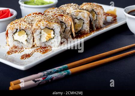 Sushi setzt Uramaki, California, Philadelphia, auf einen weißen Teller. In der Nähe Ingwer und Wasabi. Sojasauce in einer weißen Schüssel. Auf einem dunklen Hintergrund. Speicherplatz kopieren. Stockfoto