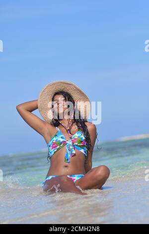 Hispanische Frau sitzt am Sandstrand und lacht mit geschlossenen Augen und Spritzwasser. Los Roques Venezuela Stockfoto