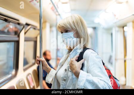 Portrait der schönen erwachsenen Frau in medizinischer Schutzmaske mit Rucksack steht in der U-Bahn und blickt nach vorne. Stockfoto