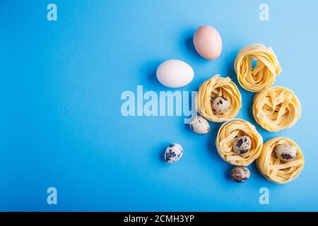 Rohe, ungekochte Tagliatelle Pasta mit Wachteleiern auf blauem pastellfarbenem Hintergrund. Draufsicht. Kopierraum. Flach liegend. Stockfoto
