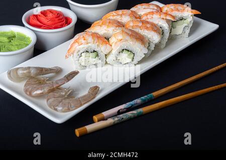 Sushi setzt Uramaki, California, Philadelphia, auf einen weißen Teller. In der Nähe Ingwer und Wasabi. Sojasauce in einer weißen Schüssel. Auf einem dunklen Hintergrund. Speicherplatz kopieren. Stockfoto