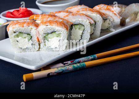 Sushi setzt Uramaki, California, Philadelphia, auf einen weißen Teller. In der Nähe Ingwer und Wasabi. Sojasauce in einer weißen Schüssel. Auf einem dunklen Hintergrund. Speicherplatz kopieren. Stockfoto