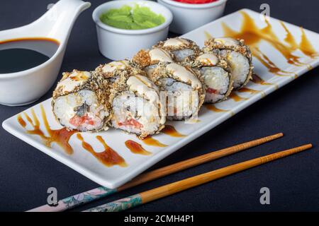 Sushi setzt Uramaki, California, Philadelphia, auf einen weißen Teller. In der Nähe Ingwer und Wasabi. Sojasauce in einer weißen Schüssel. Auf einem dunklen Hintergrund. Speicherplatz kopieren. Stockfoto