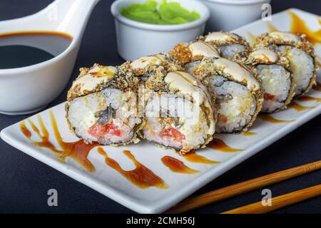 Sushi setzt Uramaki, California, Philadelphia, auf einen weißen Teller. In der Nähe Ingwer und Wasabi. Sojasauce in einer weißen Schüssel. Auf einem dunklen Hintergrund. Speicherplatz kopieren. Stockfoto