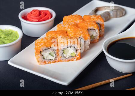 Sushi setzt Uramaki, California, Philadelphia, auf einen weißen Teller. In der Nähe Ingwer und Wasabi. Sojasauce in einer weißen Schüssel. Auf einem dunklen Hintergrund. Speicherplatz kopieren. Stockfoto