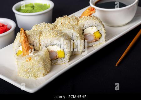 Sushi setzt Uramaki, California, Philadelphia, auf einen weißen Teller. In der Nähe Ingwer und Wasabi. Sojasauce in einer weißen Schüssel. Auf einem dunklen Hintergrund. Speicherplatz kopieren. Stockfoto