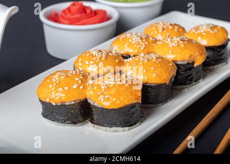 Sushi setzt Uramaki, California, Philadelphia, auf einen weißen Teller. In der Nähe Ingwer und Wasabi. Sojasauce in einer weißen Schüssel. Auf einem dunklen Hintergrund. Speicherplatz kopieren. Stockfoto