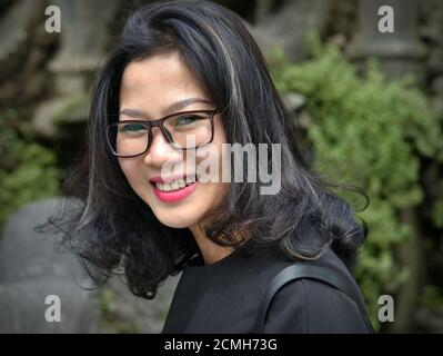 Junge attraktive fröhliche vietnamesische Frau mit großen Brillen trägt ein schwarzes Top und lächelt für die Kamera. Stockfoto