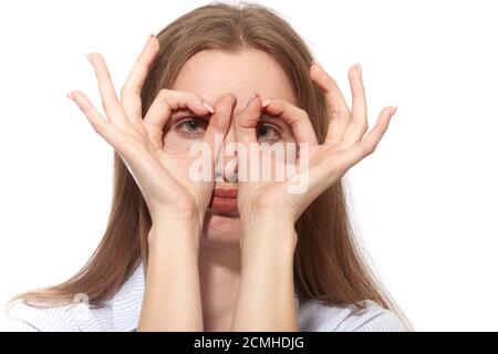 Ernsthafte junge Frau an der Kamera durch ihre Finger mit Brillen Geste auf weißem Hintergrund Stockfoto