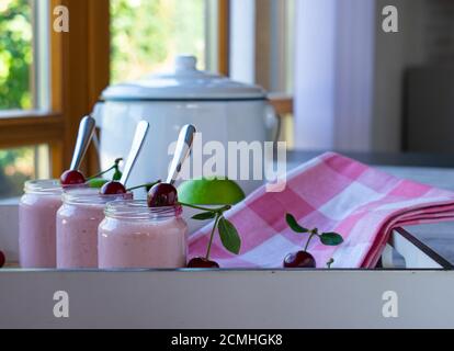 Frischer und hausgemachter Kirschjoghurt serviert in kleinen Gläsern mit Löffel auf Holztablett zu Hause Stockfoto