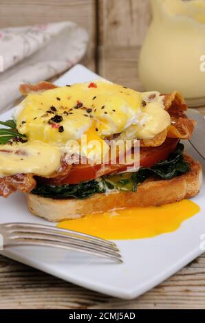 Eggs Benedict mit Scheiben Speck, Tomaten, Spinat unter die Sauce Hollandaise auf toast Stockfoto