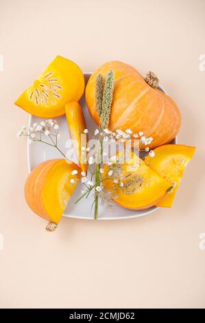 Stücke von frischem Orangenkürbis und getrockneten Blumen auf einem Weißer Teller auf hellbeigem Pastellhintergrund Stockfoto