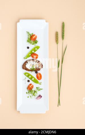 Salat aus jungen grünen Erbsen, Tomaten und Croutons mit Sahne auf einem weißen rechteckigen Teller. Stockfoto