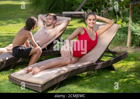 Schöne Frau in roten Badeanzug Mann und Junge hinter Stockfoto