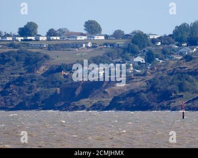 Eastchurch, Kent, Großbritannien. September 2020. Eastchurch Gap Bewohner - wo ein Haus über die Klippe ging Anfang dieses Jahres - versuchen jetzt, "die Flut zu halten" durch das Ausfüllen des Bereichs das Haus in sich selbst zusammengebrochen. Ein Bagger wurde am Rand der Klippe arbeiten gesehen, und ein Auftragnehmer wird von den Bewohnern eingesetzt, um weitere Erosion zu verzögern, wobei das Projekt von Resident Malcolm Newell, der Vorsitzender der Eastchurch Gap Cliff Erosion Community Group ist, verwaltet wird. Der orangefarbene Bagger ist in dieser Vorderansicht von Minster on Sea aus zu sehen. Kredit: James Bell/Alamy Live Nachrichten Stockfoto