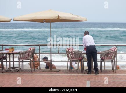 Las Palmas, Gran Canaria, Kanarische Inseln, Spanien. September 2020. Ein Kellner putzt Tische, während er auf einen fast touristenfreien Stadtstrand in Las Palmas auf Gran Canaria auf Kunden wartet. Die Kanarischen Inseln verzeichneten in den letzten 24 Stunden 190 neue Covid-Fälle. Aufgrund der aktuellen Spitze der Coronavirus-Fälle in Spanien und den kanarischen Inseln haben Großbritannien und Deutschland Spanien und die Kanarischen Inseln auf ihre Quarantäneliste gesetzt. Der Großteil der Neuinfektionen auf Gran Canaria liegt in der Hauptstadt Las Palmas. Kredit: Alan Dawson/Alamy Live Nachrichten Stockfoto