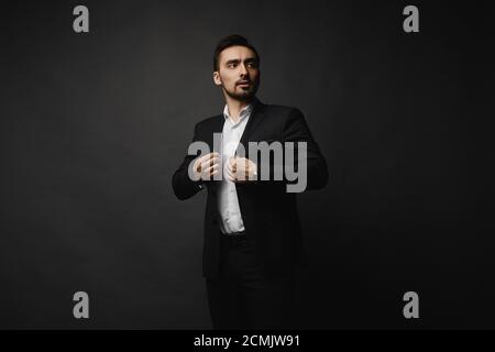 Stilvoller, hübscher Geschäftsmann in schwarzem Anzug und weißem Hemd Posiert auf dem schwarzen Hintergrund Stockfoto