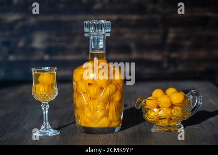 Hausgemachte Tinktur aus gelber Kirschpflaume in einer Kristallflasche und ein Weinkristall Glas auf Holzhintergrund, Ukraine, Nahaufnahme. Beeren alkoholische Getränke c Stockfoto