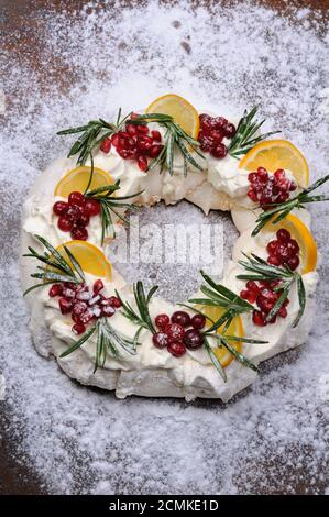 Pawlova Kuchen in Form eines Weihnachtskranzes aus Baiser mit Sahne, Granatapfel, Preiselbeere, rosem Stockfoto