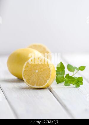 Eine halbe reife Zitrone und ein Minzzweig auf einem weißen Holztisch. Stockfoto