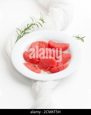 Geschälte Grapefruitscheiben und Rosmarinzweige auf einem weißen Teller auf weißem Hintergrund. Stockfoto