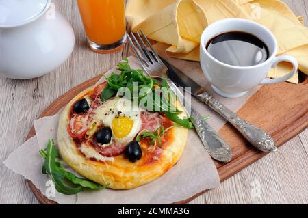 Mini-Pizza mit Wurst und Ei und Rucola, eine Tasse Kaffee zum Frühstück Stockfoto