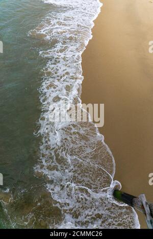 Blick hinunter auf Wellen, die auf den Sandstrand waschen, vom hölzernen Pier aus gesehen. Stockfoto