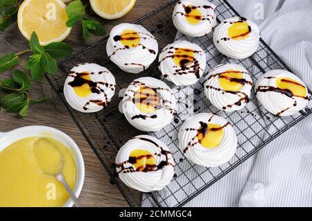 Zarte, knusprige Mini-Dessert Pavlova gefüllt mit Zitrone kurd und Schokolade Belag auf dem Rack Stockfoto