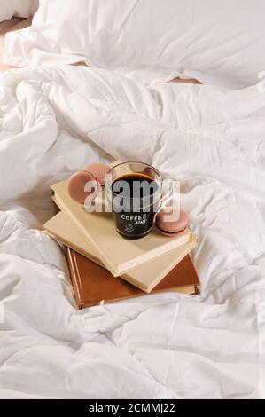 Morgendlichen Tasse Kaffee mit Schokolade Kuchen Makronen, auf einem Stapel Bücher im Bett. Stockfoto