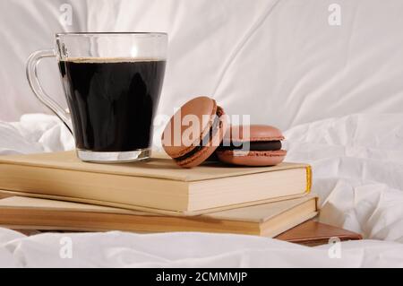 Morgendlichen Tasse Kaffee mit Schokolade Kuchen Makronen, auf einem Stapel Bücher im Bett. Stockfoto