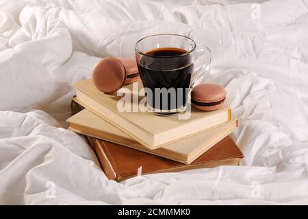 Morgendlichen Tasse Kaffee mit Schokolade Kuchen Makronen, auf einem Stapel Bücher im Bett. Stockfoto