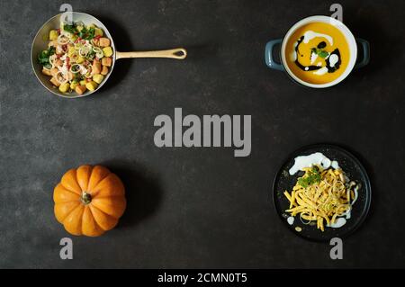 Orangefarbener Kürbis auf schwarzem Hintergrund mit Kürbisrezepten, Pasta, Gnocchi und Kürbissuppe, Herbstfrüchte mit leuchtenden Farben Stockfoto