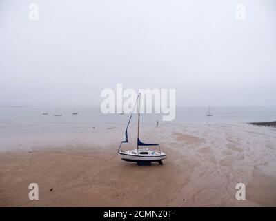 Eine Flossenkielyacht am Strand bei Ebbe an einem nebligen Tag in den Mumbles, Swansea Bay, Wales Großbritannien Stockfoto