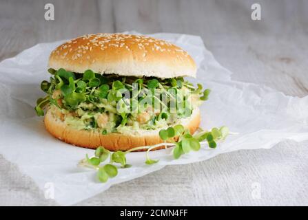 Ein vegetarischer Burger aus einem glutenfreien Brötchen mit Kichererbsen, Avocado und Kräutern, Rettichsprossen. A Stockfoto