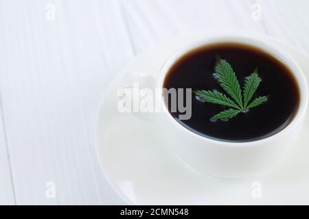 Weiße Tasse Cannabis-Kaffee mit Hanfblättern aus der Nähe Stockfoto