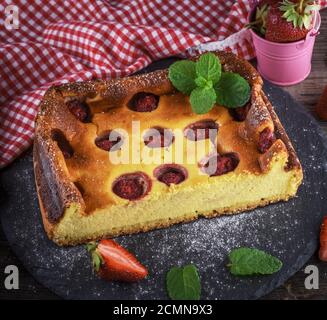 Die Hälfte einen Käsekuchen mit Erdbeeren auf schwarzem Graphit Platte Stockfoto