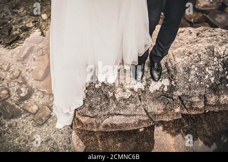 Die Beine der Braut und des Bräutigams stehen auf dem großen grauen Stein Stockfoto