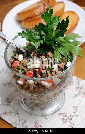 Gehackter Thunfisch mit Ei, Tomatenwürfel und Olivenscheiben, Kapern und Petersilie. Salat in einem Glas Stockfoto