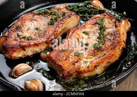 Saftig, brüniert Schweinesteak auf einen Knochen in Öl mit Knoblauch und Kräutern, die in der Pfanne. Close-up. Stockfoto