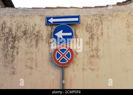 Altes blaues metallisches Pfeilschild gegen eine beschädigte Betonwand Zeigt an, dass man nach links geht und kein Parkschild Stockfoto