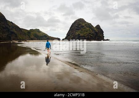 Junger Mann, der mit Schuhen am Piha Strand läuft Seine Hände und Spiegelung auf dem nassen Sand Stockfoto