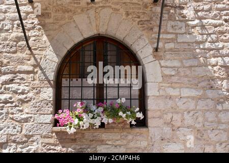 Ein Korb mit leuchtend rosa und roten Blumen hängt an Das Fenster eines Hauses in einem alten Gebäude in Italien Stockfoto