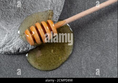 Holzlöffel für Honig und verschütteten Honig auf einem grauen Zement Hintergrund. Stockfoto