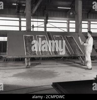 1960er Jahre, historisch, in einer Fabrik aus vorgegossenem Beton, England, Großbritannien, ein Arbeiter mit einer Betonfertigteilplatte in einer Form. In dieser Zeit gab es einen Boom in der Konstruktion von Hochhäusern und der so genannten 'brutalen' Architektur. Die Paneele wurden außerhalb des Standorts in einer kontrollierten Fabrikumgebung vorbereitet, gegossen und ausgehärtet, wodurch die Baukosten günstiger und schneller wurden, da die Kosten für qualifizierte Arbeitskräfte und Materialien vor Ort reduziert wurden. Auch da der Beton außerhalb der Baustelle hergestellt wurde, ließ er Zeit, ihn zu stärken, bevor er auf die Baustelle verlegt wurde. Stockfoto