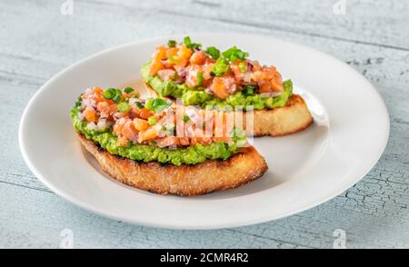 Zwei Guacamole und Lachs Toasts auf weißem Teller Stockfoto
