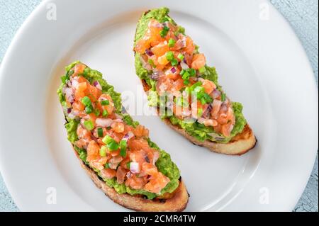 Zwei Guacamole und Lachs Toasts auf weißem Teller Stockfoto