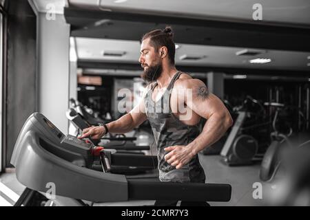 Ein erwachsener, bärtiger Mann, der im Fitnessstudio auf dem Laufband läuft. Stockfoto