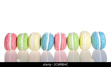 Reihe von Macaron Cookies seitlich Seite an Seite mehrere Pastellfarben und Aromen isoliert auf weiß, Reflexion auf dem Tisch. Traditionelles französisches Vergnügen. Stockfoto